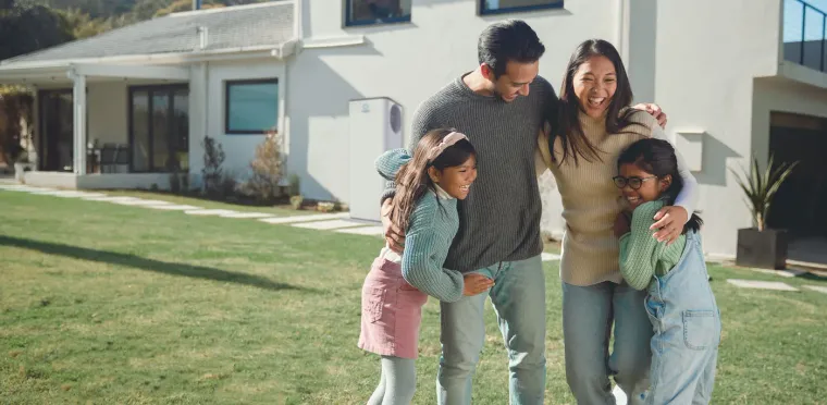 Family outside their home with an Emerald heat pump on the wall behind them